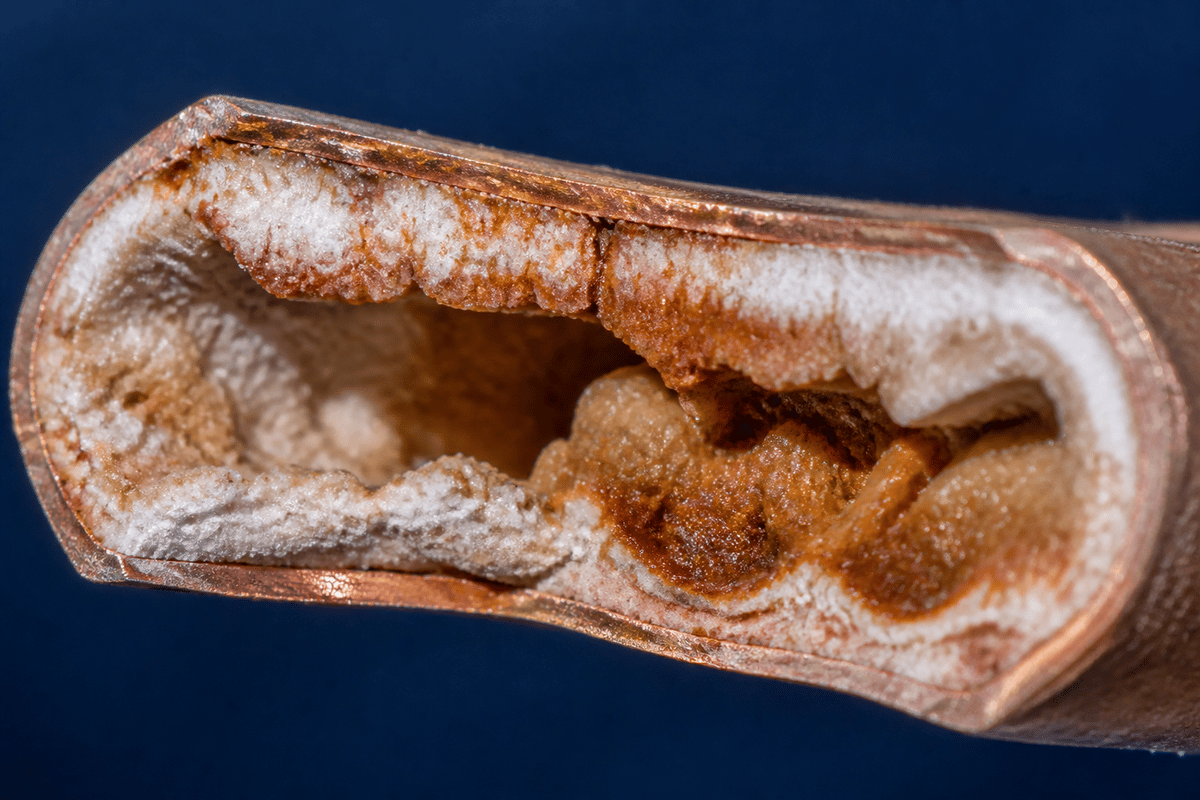 Copper pipe cut open showing its interior packed with mineral limescale buildup